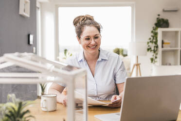 Smiling female entrepreneur with document sitting at desk - UUF22918