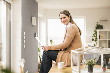 Female entrepreneur with laptop sitting on desk at home - UUF22941