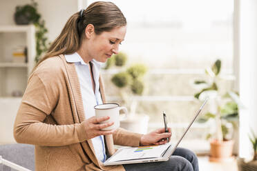 Geschäftsfrau schreibt auf einem Dokument und hält eine Kaffeetasse - UUF22943
