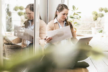 Businesswoman examining document while using digital tablet - UUF22949