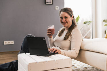 Happy woman drinking juice sitting in living room at home - UUF22956