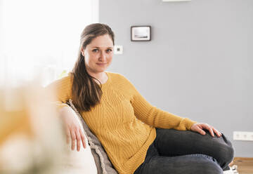Frau in gelbem Pullover sitzt zu Hause auf dem Sofa - UUF22963