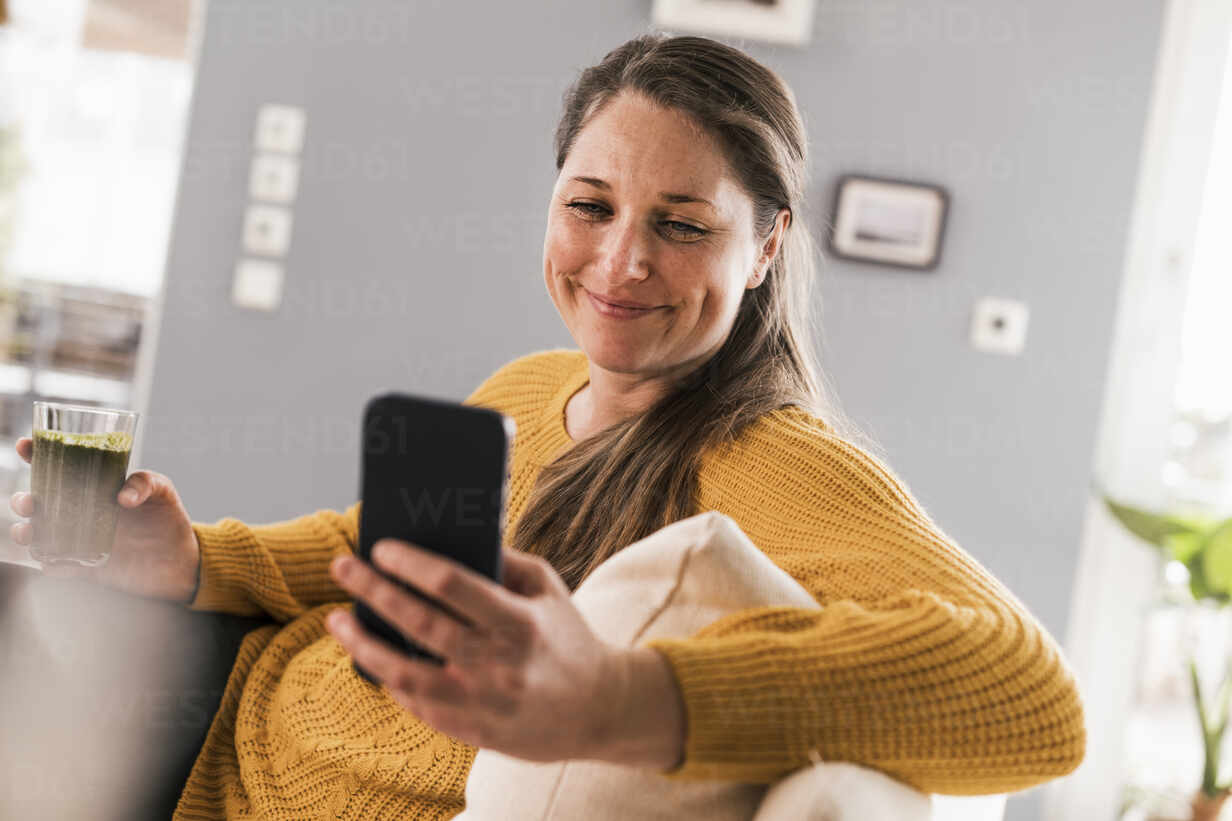 Happy mid adult woman using mobile phone in living room stock photo