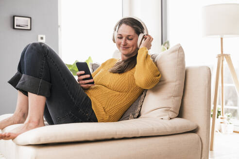 Entspannte Frau genießt Musik, während sie auf dem Sofa im Wohnzimmer sitzt - UUF22969