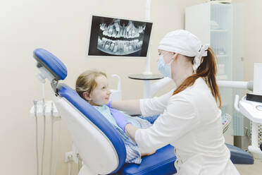 Eine Zahnärztin legt ein Tuch über ein kleines Mädchen, das im Zahnarztstuhl sitzt - EYAF01539