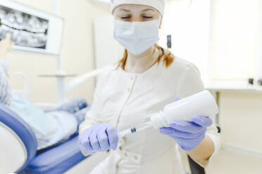 Female dentist wearing protective face mask preparing syringe for injection - EYAF01542