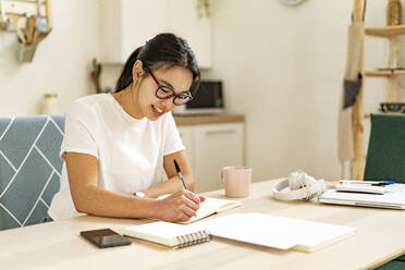 Smiling woman writing in book at home - GIOF11677