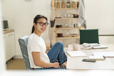 Young smiling woman sitting by table at home - GIOF11679