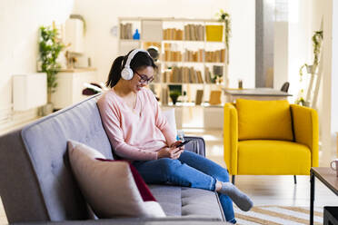 Smiling woman with headphones using mobile phone at home - GIOF11689