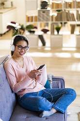 Woman with headphones and mobile phone smiling while sitting at home - GIOF11692