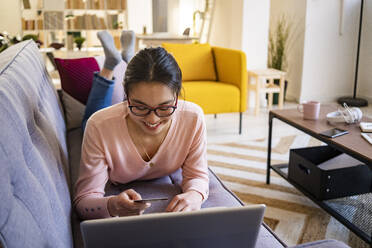 Junge Frau mit Kreditkarte beim Online-Shopping auf dem Laptop zu Hause - GIOF11706