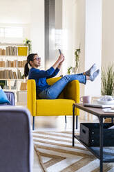 Young woman taking selfie through mobile phone while sitting at home - GIOF11717