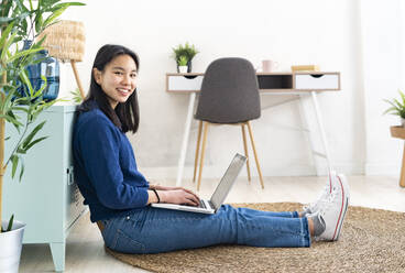 Young smiling woman with laptop sitting on jute rug at home - GIOF11732