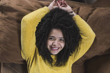 Cheerful curly haired woman lying on sofa at home - DSIF00362