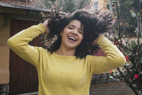 Cheerful woman playing with curly black hair at back yard - DSIF00365
