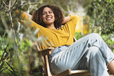 Lächelnde Frau, die sich im Frühling im Gartenstuhl in einem nachhaltigen Bio-Gemüsegarten entspannt - SBOF03091