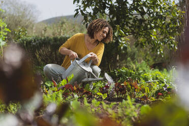 Smiling woman watering plants in permaculture garden - SBOF03141