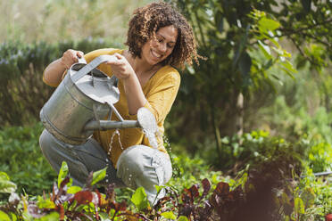 Happy woman watering plants in permaculture garden - SBOF03143