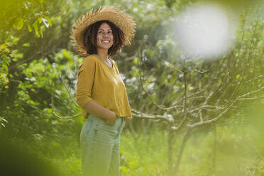 Smiling woman in straw hat looking away while standing in garden - SBOF03147