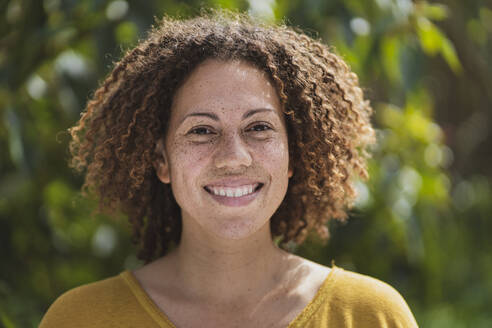 Smiling curly haired woman with freckles in vegetable garden - SBOF03150