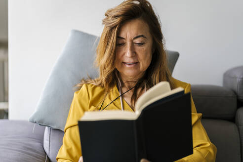 Frau liest ein Buch, während sie zu Hause auf dem Sofa sitzt - EGAF02061