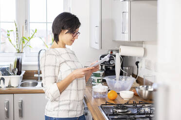 Woman reading a recipe before baking cake at home - WPEF04205