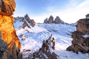 Mann auf Felsen mit Blick auf den verschneiten Monte Paterno und die Drei Zinnen bei Sonnenuntergang, Sextner Dolomiten, Südtirol, Italien, Europa - RHPLF19356