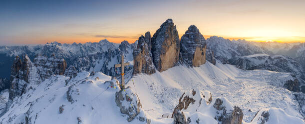 Gipfelkreuz auf dem schneebedeckten Monte Paterno mit den Drei Zinnen im Hintergrund bei Sonnenuntergang, Sextner Dolomiten, Südtirol, Italien, Europa - RHPLF19362