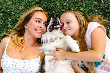 From above of delighted woman and girl hugging cute fluffy Border Collie dog while lying on grass on meadow in park - ADSF21214