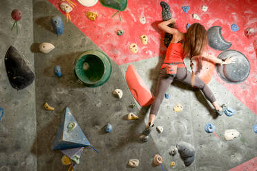 Rückenansicht einer starken Sportlerin in Sportkleidung beim Klettern an einer Wand in einem modernen Boulderzentrum - ADSF21221