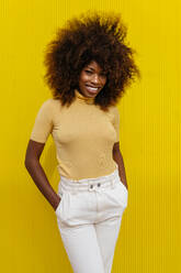 Porträt einer lockig behaarten schwarzen Frau, die vor einem gelben Hintergrund in die Kamera schaut - ADSF21242