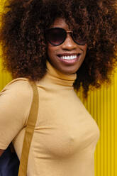 Portrait of a curly haired black woman looking at camera in front of a yellow background - ADSF21245