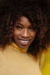Porträt einer lockig behaarten schwarzen Frau, die vor einem gelben Hintergrund in die Kamera schaut - ADSF21246