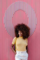 Black woman with afro hair posing in front of a pink wall looking away - ADSF21256