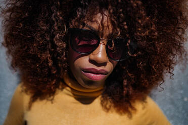 Black woman with afro hair posing in front of a gray wall looking at camera - ADSF21262