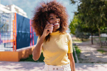 Schwarze Frau mit Afrofrisur telefoniert beim Gehen auf der Straße - ADSF21264