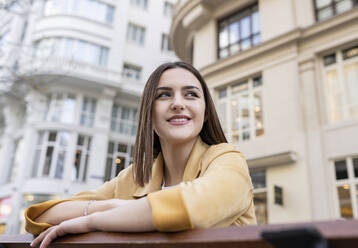 Smiling young woman with brown hair looking away in front of building - JCCMF01403