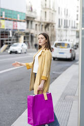 Frau mit Einkaufstaschen, die auf dem Bürgersteig stehend ein Taxi ruft - JCCMF01410