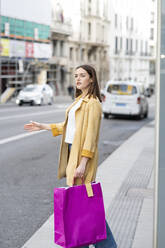 Woman with shopping bags hailing taxi while standing on sidewalk - JCCMF01410