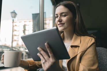 Junge Frau benutzt ein digitales Tablet, während sie in einem Café sitzt - JCCMF01416