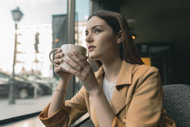 Schöne Frau trinkt Kaffee und schaut durch das Fenster eines Cafés - JCCMF01419