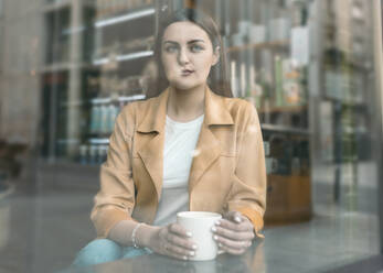 Young beautiful woman seen through glass window sitting at cafe - JCCMF01420