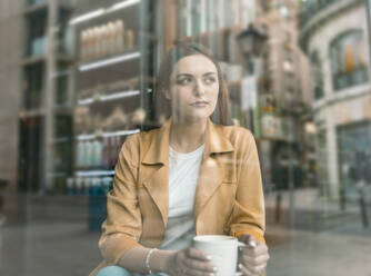 Thoughtful young woman sitting at cafe seen through glass window - JCCMF01421