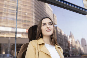 Smiling young woman standing in front of glass wall looking away - JCCMF01427