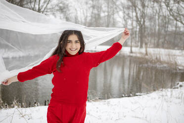 Fröhliche Frau spielt mit Tuch gegen See im Winter - AXHF00185