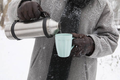 Mann gießt im Winter Tee in einen Becher - AXHF00197