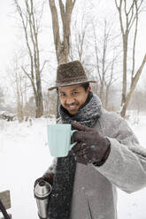 Mann hält Teetasse, während er im Winter auf verschneitem Land steht - AXHF00199