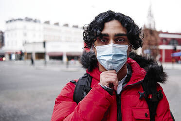 Junger Mann in wattierter Jacke mit Gesichtsschutzmaske während COVID-19 - ASGF00044