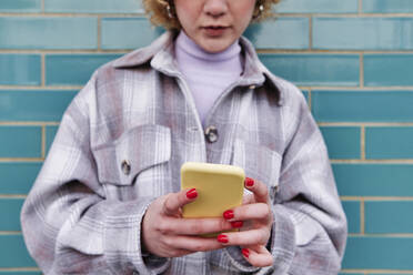 Junge Frau, die ein Mobiltelefon an der Wand benutzt - ASGF00047