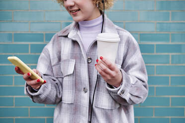 Lächelnde Frau mit Einweg-Kaffeebecher und Mobiltelefon - ASGF00071